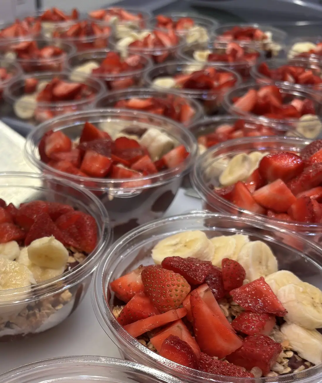 Trays of açaí bowls topped with strawberries and banana for a catering order